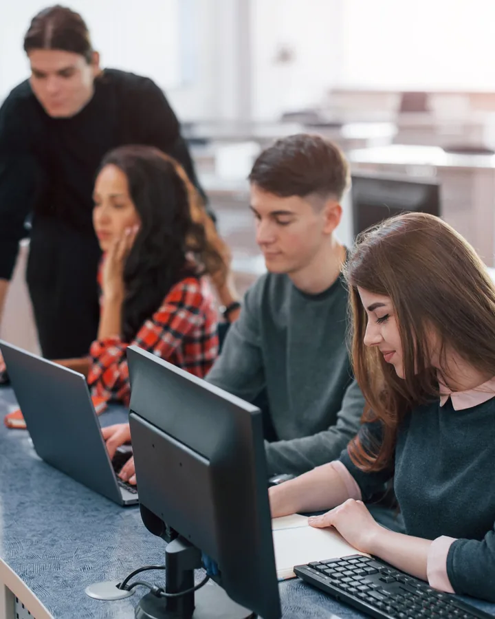 Students working at computers in a classroom with a tutor